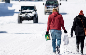 two people walk through snow carrying groceries as vehicles approach in the other direction