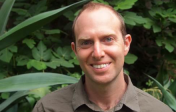 headshot of Asher Price in front of green foliage